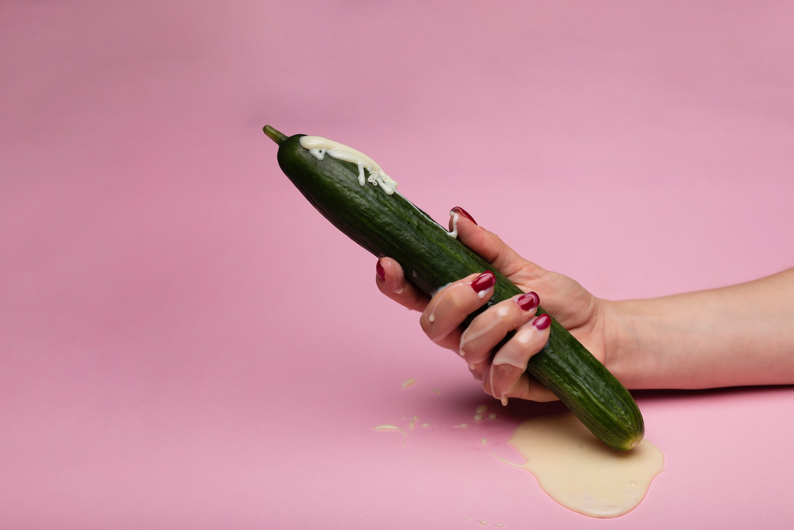 person holding green cucumber on pink surface